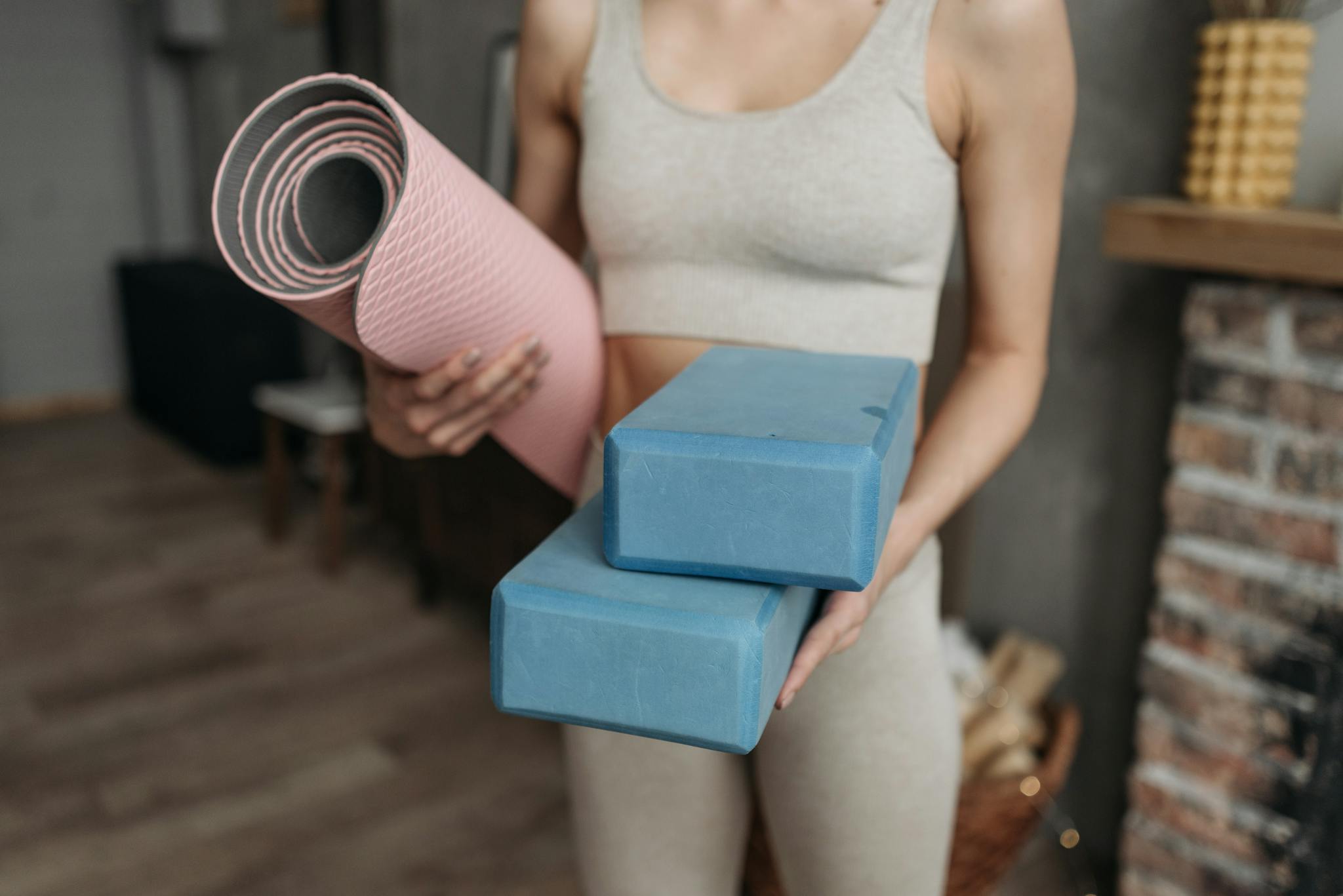 Woman holds yoga mat and blocks indoors, highlighting fitness routine at home with modern active wear.