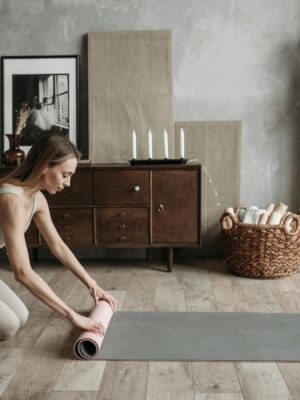 Woman rolling out a yoga mat in a cozy and stylish home interior, ready for a workout session.
